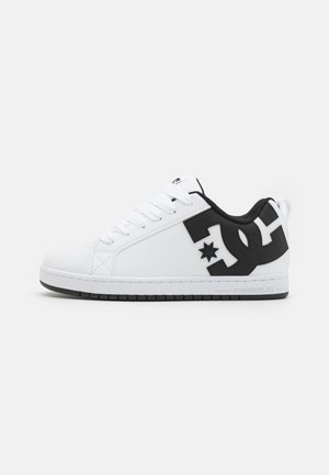 Biały niski sneaker z czarnym logo DC po boku, białe sznurówki, czarna podszewka i czarna gumowa podeszwa.