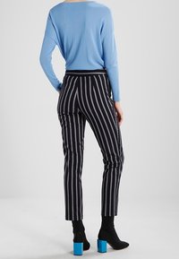 Blå långärmad topp i kombination med svartvitrandiga byxor. Byxorna har en åtsittande design och ankellängd, tillsammans med klackskor.