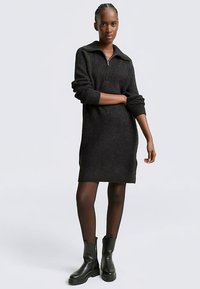 Czarna dzianinowa sukienka z kołnierzem na zamek, prążkowaną fakturą i podwiniętymi rękawami, zestawiona z czarnymi botkami do kostki.