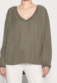Maglietta verde oliva a maniche lunghe con scollatura a V profonda e vestibilità comoda. Realizzata in tessuto morbido, presenta maniche ampie e un orlo dritto.