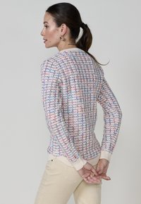 Gilet texturé en crème, motif tissé multicolore avec des accents bleus, rouges et violets. Manches côtelées et ourlet, design ajusté.