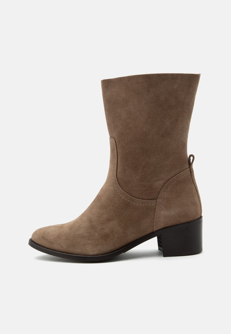 Bottine en daim marron mi-hauteur avec bout arrondi, petit talon empilé, couture latérale et languette arrière sur fond blanc.