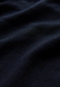 Tamno plava tkanina s mekom, glatkom teksturom, koja sadrži istaknute nabore i pregibe koji naglašavaju njezinu draperiju i težinu.
