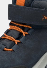 Niebieski syntetyczny but w stylu high-top z pomarańczowymi sznurówkami i akcentami, wyprofilowanym kołnierzem oraz teksturowaną powierzchnią. Pasek na rzep nad sznurówkami.