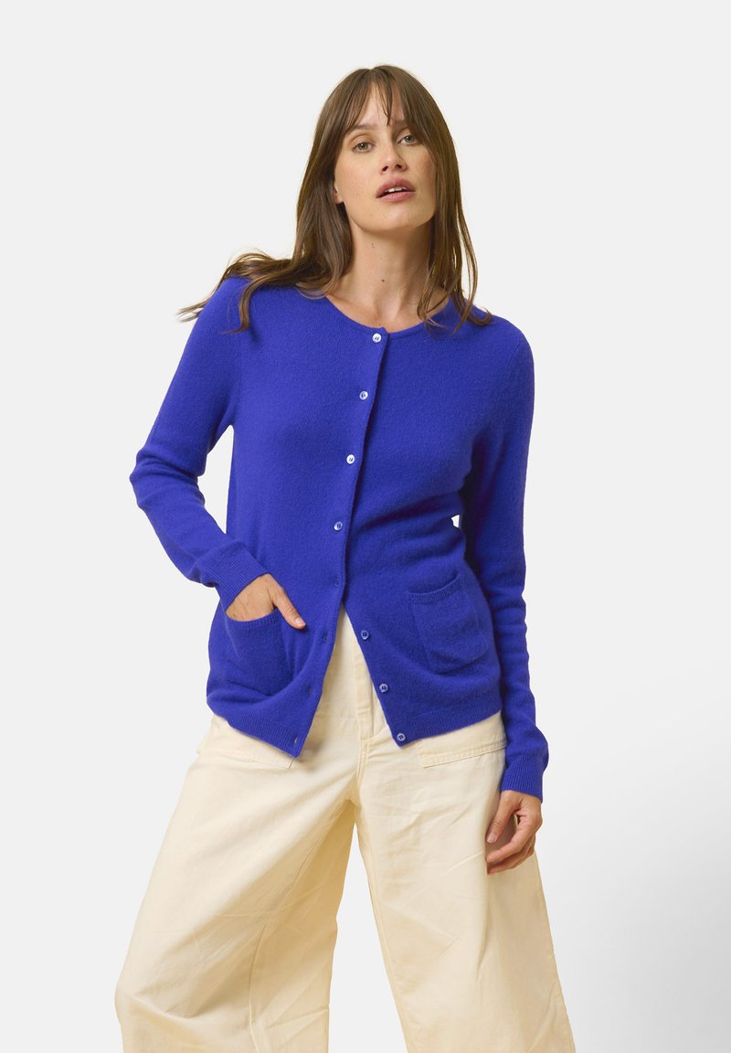 Cardigan blu, leggero, con maniche lunghe, scollo rotondo e due tasche frontali. Presenta chiusura a bottoni e una consistenza morbida.