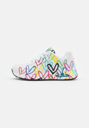 Witte sportieve schoen met kleurrijke hartpatronen in rood, geel, groen en blauw, met een zwarte zool en luchtkussendetails.