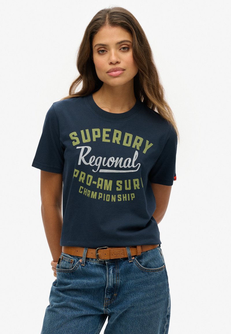 Camiseta de algodón de color navy con mangas cortas, con grandes letras en blanco y verde que dicen "Campeonato Regional Pro-Am de Surf SUPERDRY".
