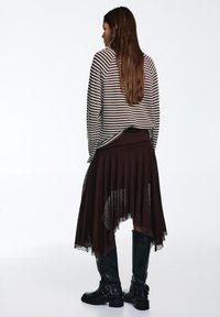 Striped long-sleeve shirt in brown and cream, layered over a dark brown skirt with lace trim, paired with knee-high black boots.