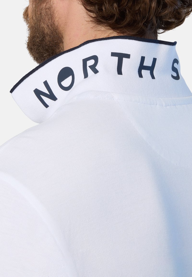 Camisa polo blanca con un alto cuello, letras negras "NORTH S", tejido texturizado y detalles en azul marino en el borde del cuello.