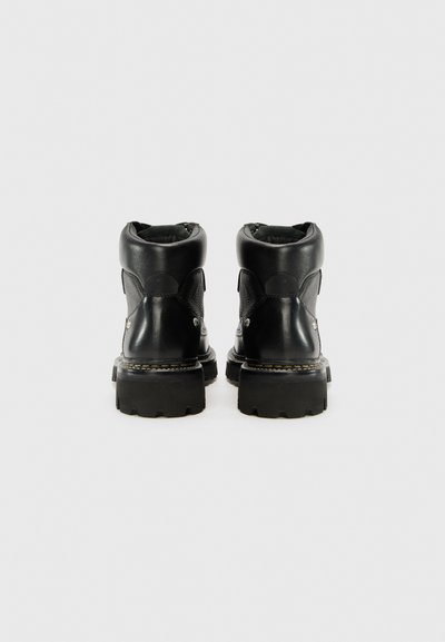 Botas tobilleras de cuero negro con un acabado texturizado, suela de goma, cuello acolchado y detalles de metal. Diseñadas para la durabilidad.
