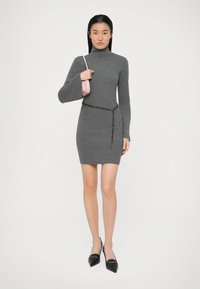 Grå ribbet strikket kjole med en mock turtleneck og lange ærmer, accentueret af et kædebælte. Sorte spidse flade sko og en lille pink håndtaske.
