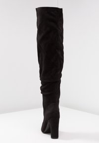 Botas negras sobre la rodilla hechas de suave ante, con un tacón afilado, diseño holgado y textura lisa sin hardware visible.