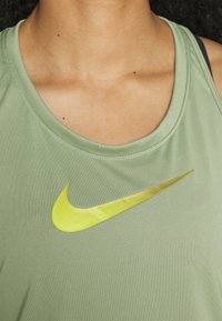 Canottiera sportiva verde chiaro con una texture morbida, dotata di un logo Nike giallo lucido sul davanti e un classico scollo rotondo.