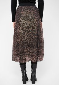 Leren rok met luipaardprint van doorschijnende stof, voorzien van een zwarte tailleband, gelaagd ontwerp en een vloeiende silhouette. Gecombineerd met zwarte enkellaarsjes.