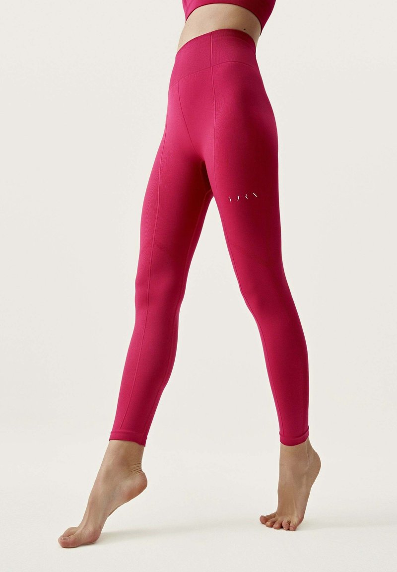 Leggings ajustados de cintura alta en tejido rosa brillante, con costuras tonales y pequeños acentos blancos en el muslo izquierdo. Textura suave.