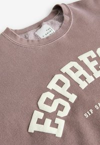 Felpa color malva chiaro con colletto tondo, caratterizzata da audaci lettere bianche in maiuscolo che formano la parola "ESPRESSO" e un'etichetta con la scritta "THE T-SHIRT GUY."