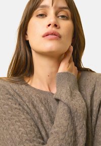 Brązowy sweter w splot kablowy o luźnym kroju, z szerokim dekoltem i ściągaczami. Miękka tekstura z przytulnym wyglądem.