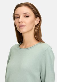 Hellgrüner Pullover mit rundem Ausschnitt, langen Ärmeln und weicher Textur. Minimales Design mit glatter Oberfläche und ohne sichtbare Muster oder Akzente.