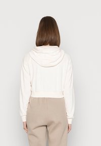 Beskuvad krämvit hoodie med en vikt huva, ribbade ärmar och nederkant. Mjuk textur, avslappnad passform och minimalistisk design.