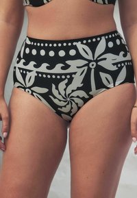 Bas de bikini taille haute noir avec de grands motifs floraux et des pois blancs, présentant une texture lisse et un ajustement snug.
