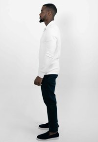 Witte lange mouwen polo, donkere slim-fit broek, zwarte instap schoenen. Eenvoudig ontwerp, gladde textuur, zijaanzicht tegen een witte achtergrond.