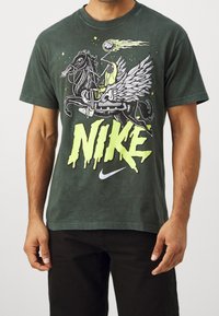 Camiseta de algodón verde con un diseño gráfico de un caballo alado y una pelota de baloncesto, con el texto "NIKE" en amarillo brillante y el logo en blanco.