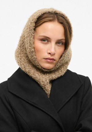 Écharpe-capuche beige en tricot avec une finition douce et texturée, portée sur un manteau noir. Le design couvre la tête et le cou pour apporter de la chaleur.