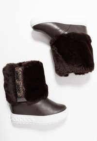 Botas de cuero marrón con una suela plataforma blanca, que cuentan con un suave puño de piel marrón y un detalle de tela estampada en el lateral.