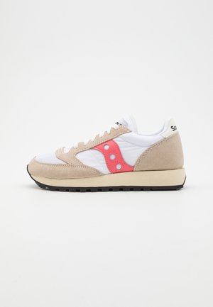 Biały i beżowy sneaker z czerwonym logo po boku, sznurowany z przodu, czarną podeszwą i wyściełanym kołnierzem na jednolitym białym tle.