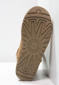 Semelle de bottine en suède marron présentant un motif texturé en zigzag avec un logo central et un design circulaire. Forme plate et large offrant une stabilité optimale.