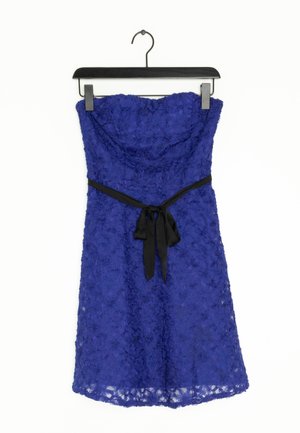 Trägerloses königsblaues Spitzenkleid mit einem schwarzen Satinschleifenband in der Taille, hängend an einem schwarzen Kleiderbügel vor weißem Hintergrund.