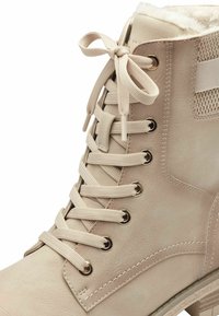 Bottine beige avec une finition texturée, dotée d'œillets dorés et de lacets beige, doublure douce et un petit talon surélevé.