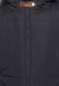 Svart isolerad jacka med dragkedja, med läderdetalj vid halsen och horisontell sömnad. Slät textur, inga mönster.