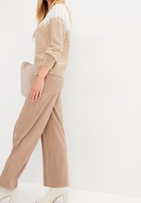 Beiger Pullover mit weißem Spitzensteg, kombiniert mit lockeren beigen Hosen und cremefarbenen Knöchelstiefeln. Einfaches Design mit sanften Texturen.
