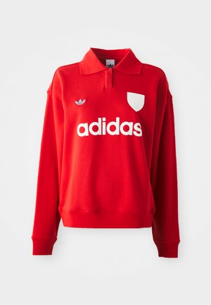 Rød hettegenser med krage, hvit "adidas" logo foran, og en hvit skjoldlapp. Har et blått adidas-emblem på skulderen.