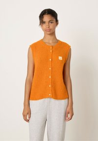 Oranje mouwloze gebreide top met een ronde halslijn, voorzien van een knoopsluiting en een klein label aan de linkerkant. Zachte, gestructureerde stof.