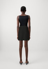 Sort bodysuit med tynde stropper parret med en sort mini-skirt med lynlås i ryggen. Modellen står med ryggen til kameraet foran en ensfarvet baggrund.