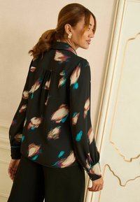 Fekete blúz könnyű anyagból, absztrakt, színes mintákkal bézs, kék és bordó színekben; hosszú ujjú és klasszikus gallérral.