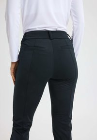 Zwarte sportbroek met een aansluitend ontwerp, een gladde textuur en contrasterende stiksels. Bevat twee achterzakken en een middelhoge tailleband.