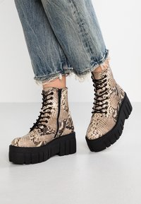 Stivaletti con lacci in un motivo a stampa pitone beige e marrone, con una robusta suola nera a piattaforma e cerniera laterale per facilitare la calzata.