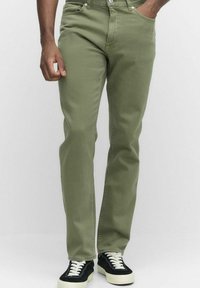 Olivgröna jeans tillverkade av bomull, med rak skärning och en slät textur. Modellen bär svarta sneakers med vita sulor.