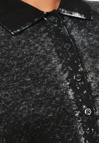 Prim-plan cu un tricou tricotat în două nuanțe de negru și gri, cu un guler striat și patru nasturi negri pe partea din față.