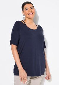 Mörkblå topp med kort ärm och rundad halsringning, med två axelremmar. Slen textur och avslappnad passform, matchad med neutrala byxor.