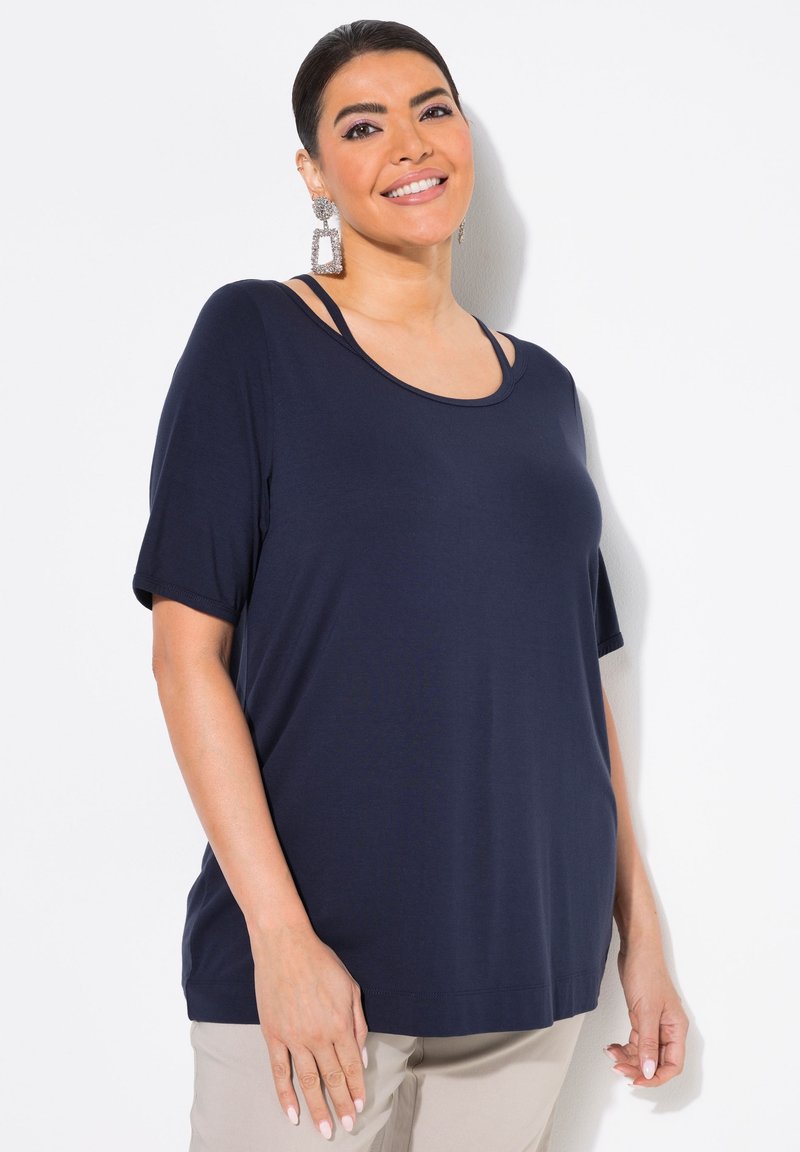 Mörkblå topp med kort ärm och rundad halsringning, med två axelremmar. Slen textur och avslappnad passform, matchad med neutrala byxor.