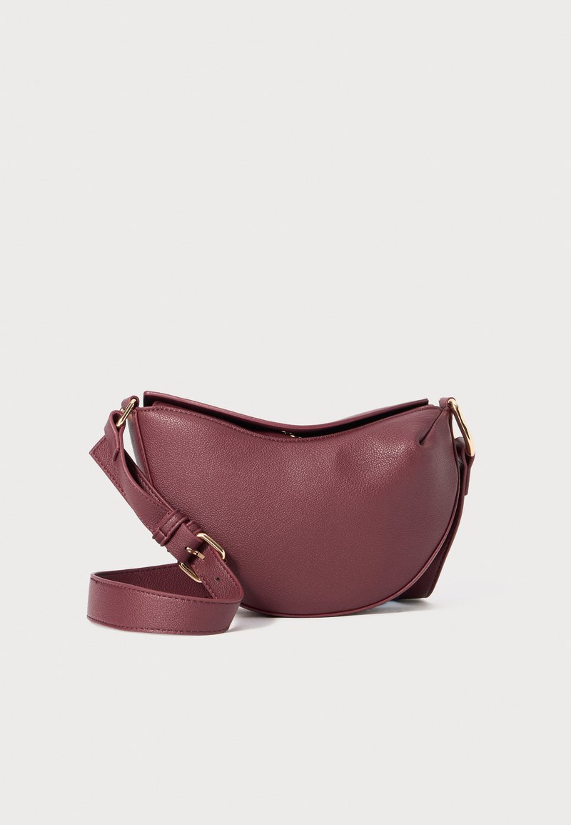 Sac en cuir bordeaux rond avec une surface texturée, une bandoulière réglable et des accents en métal doré ; conçu en forme de demi-lune.