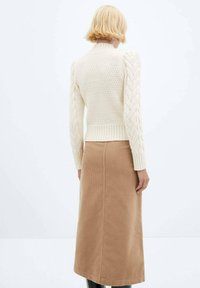 Pull crème en maille avec un corps texturé et des manches à torsades, associé à une jupe en velours côtelé beige, vue de dos.