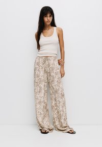 Débardeur beige et pantalons à jambes larges avec un imprimé léopard marron clair, fabriqués dans un tissu doux et fluide avec une taille élastique et un cordon de serrage.