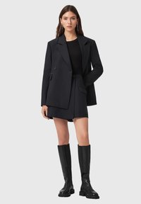 Zwarte oversized blazer met een op maat gemaakte pasvorm, gecombineerd met een bijpassende mini-jurk en zwarte kniehoge laarzen. Gladde stof en gestructureerd ontwerp.