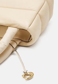 Beżowa skórzana torba na ramię z wyściełanym wzorem, zaokrąglonymi uchwytami oraz złotym zapięciem na skórzanym pasku.