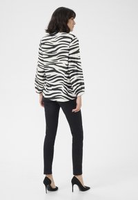 Svart och vit zebra-mönstrad blus med vida ärmar, parat med svarta slim-fit byxor och svarta högklackade skor.